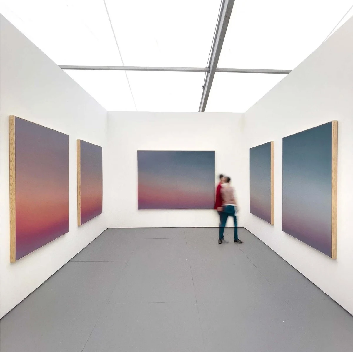 A fair booth hung on three walls with sunset-toned canvases, a visitor standing before the largest of them.