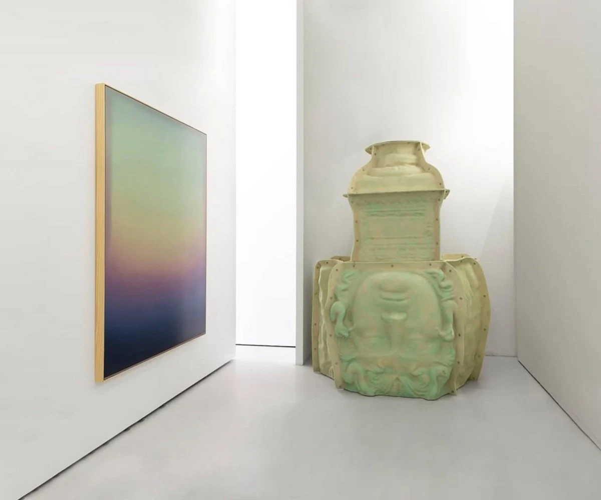 A green and violet painting on a white wall, beside a large pale celadon vessel standing on the floor.