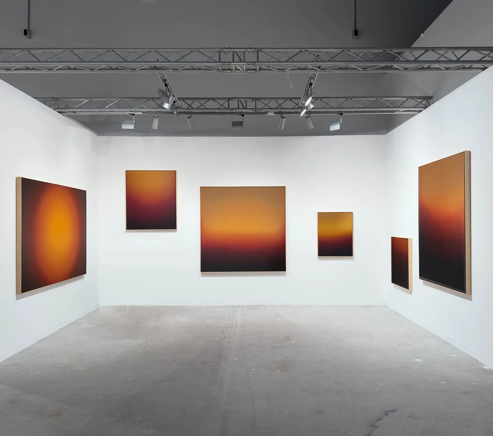 A high industrial hall under a lighting truss, six paintings of amber and deep blue hung around white walls.