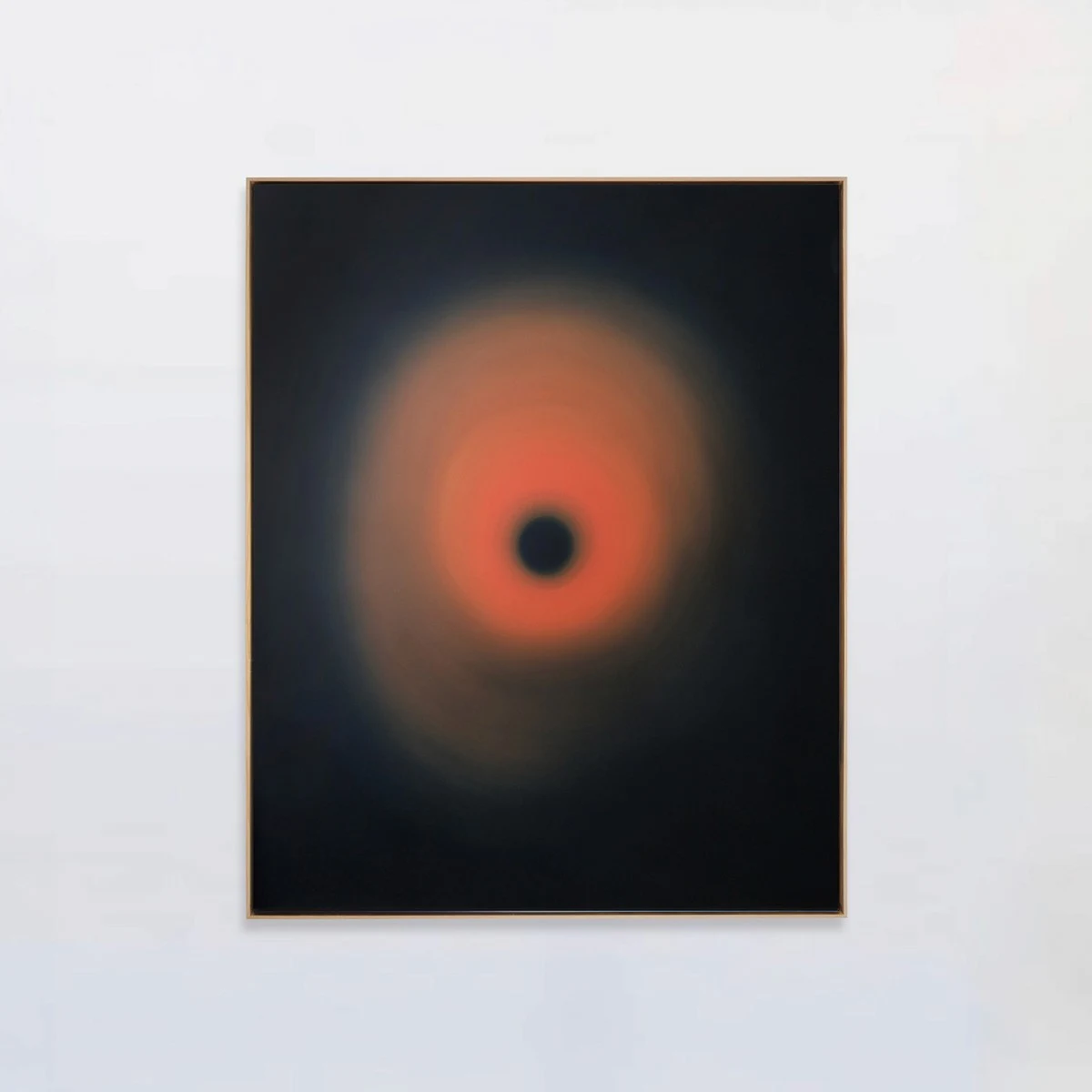 A framed dark panel holding a burning orange halo around a small black centre, alone on a white wall.