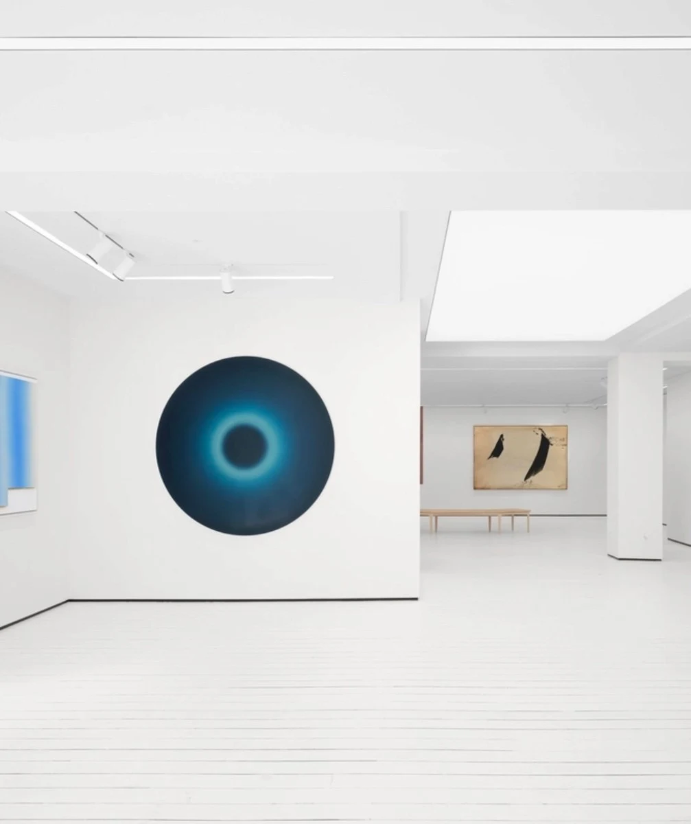 A white gallery seen through an opening, a circular blue painting on the far wall and the room continuing beyond.