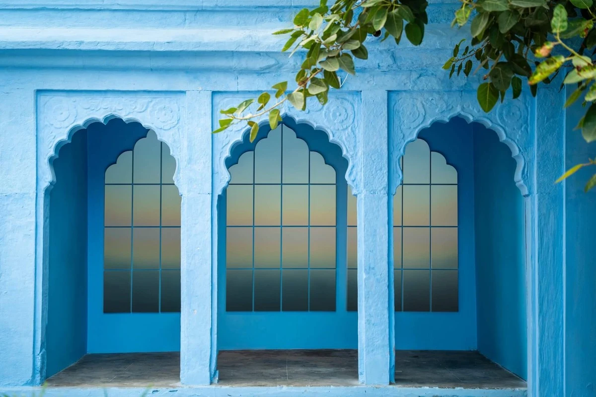 A blue-painted arcade of scalloped arches, a graded panel set into each opening, leaves hanging over the top.