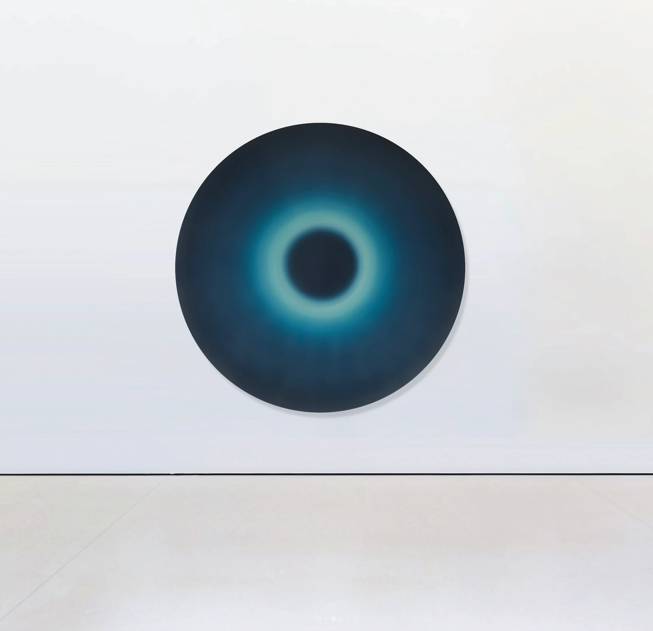 A circular painting, deep blue-black around a luminous pale ring that encircles a dark centre.