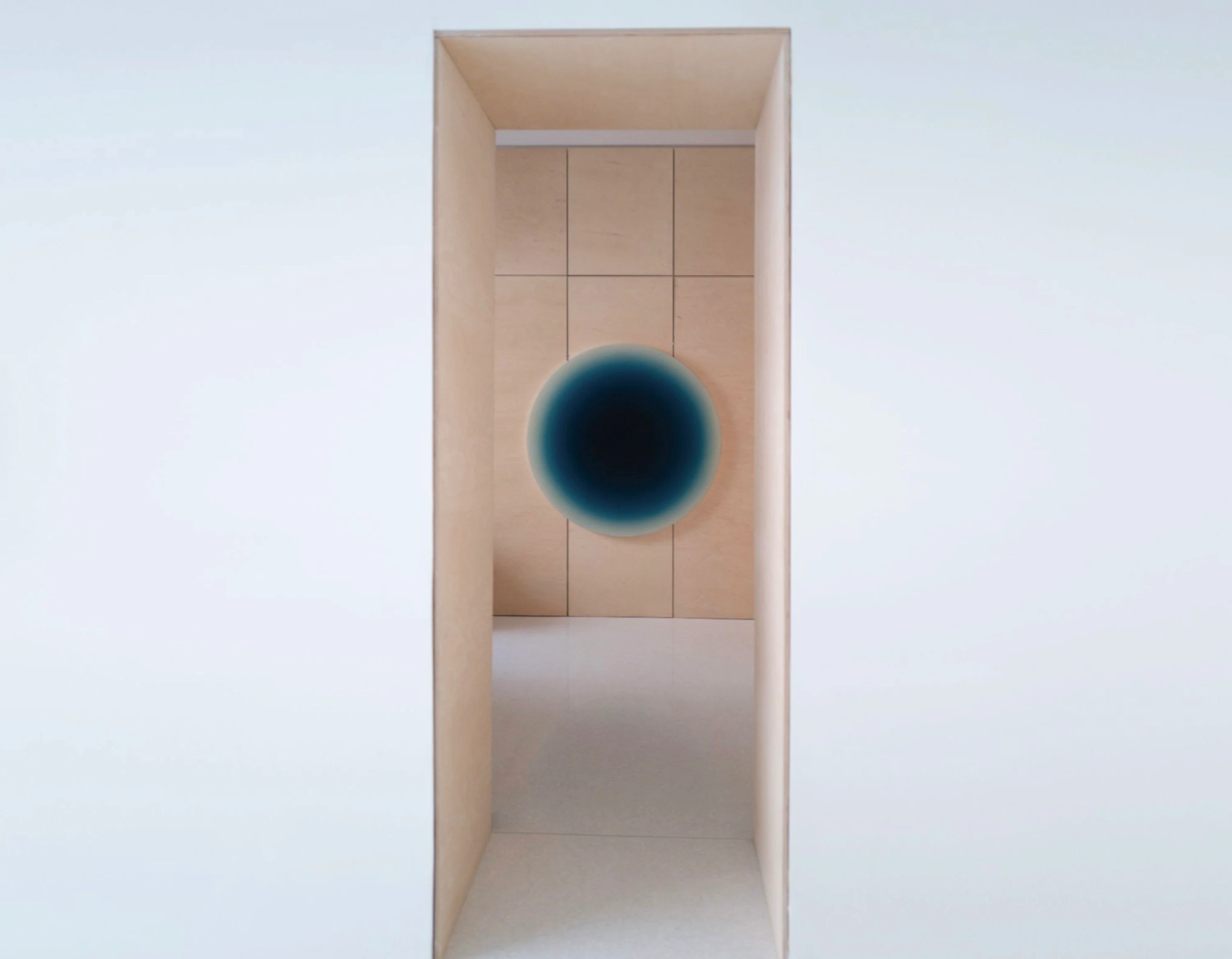 A circular blue painting glowing at the end of a narrow plywood corridor, seen through the opening.