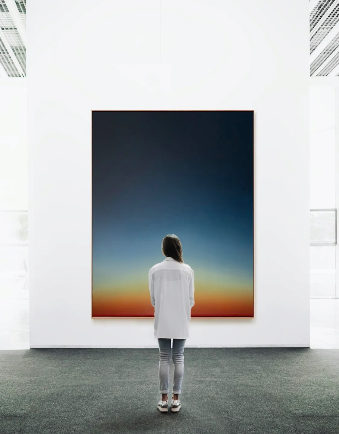 A tall painting in a fair booth, deep night blue at the top burning down into orange and red at the base; a visitor stands before it, looking up.
