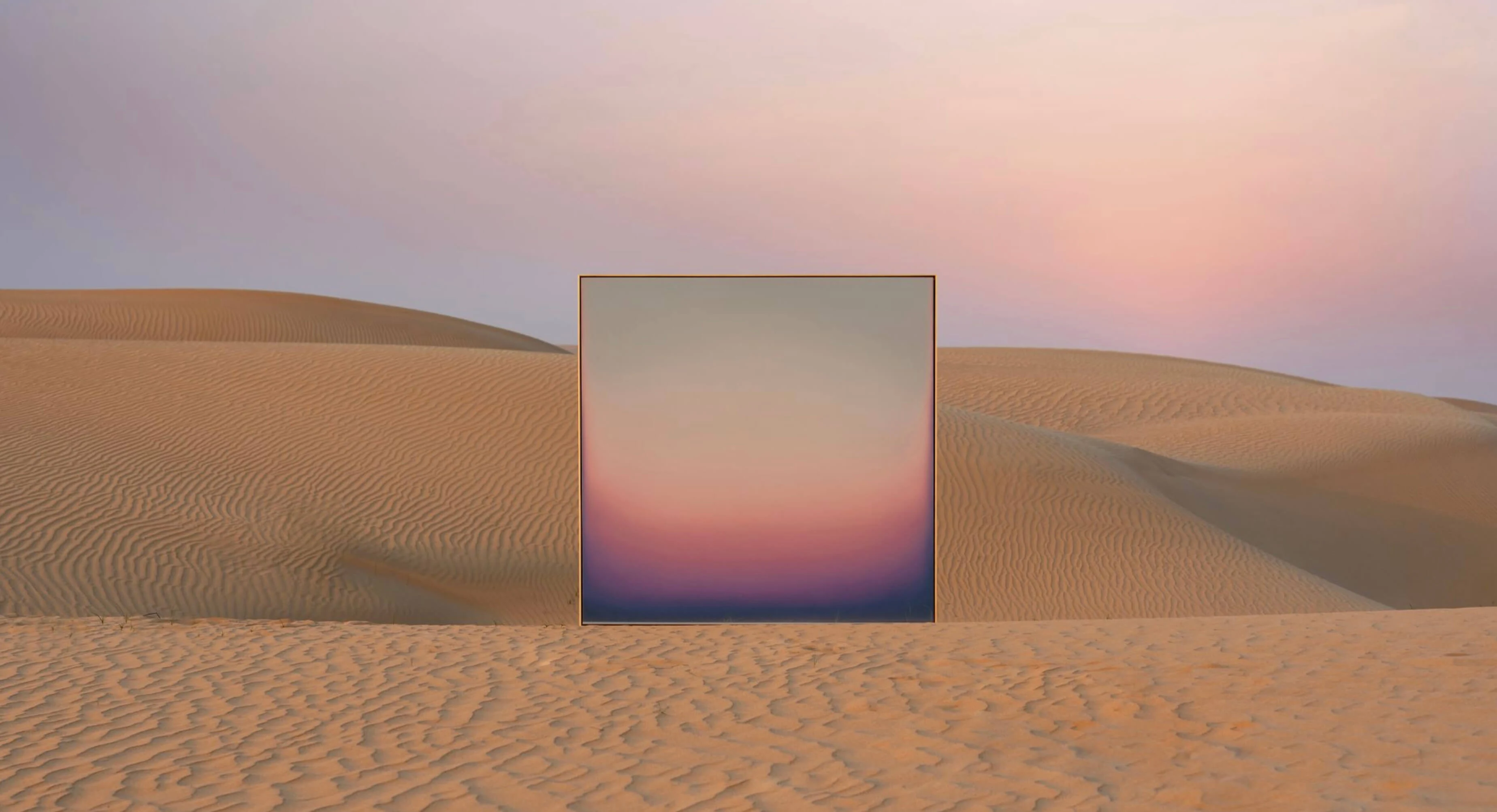 A square painting standing upright in desert dunes at dusk, its pale gold top sinking through lilac into deep blue, echoing the sky behind it.