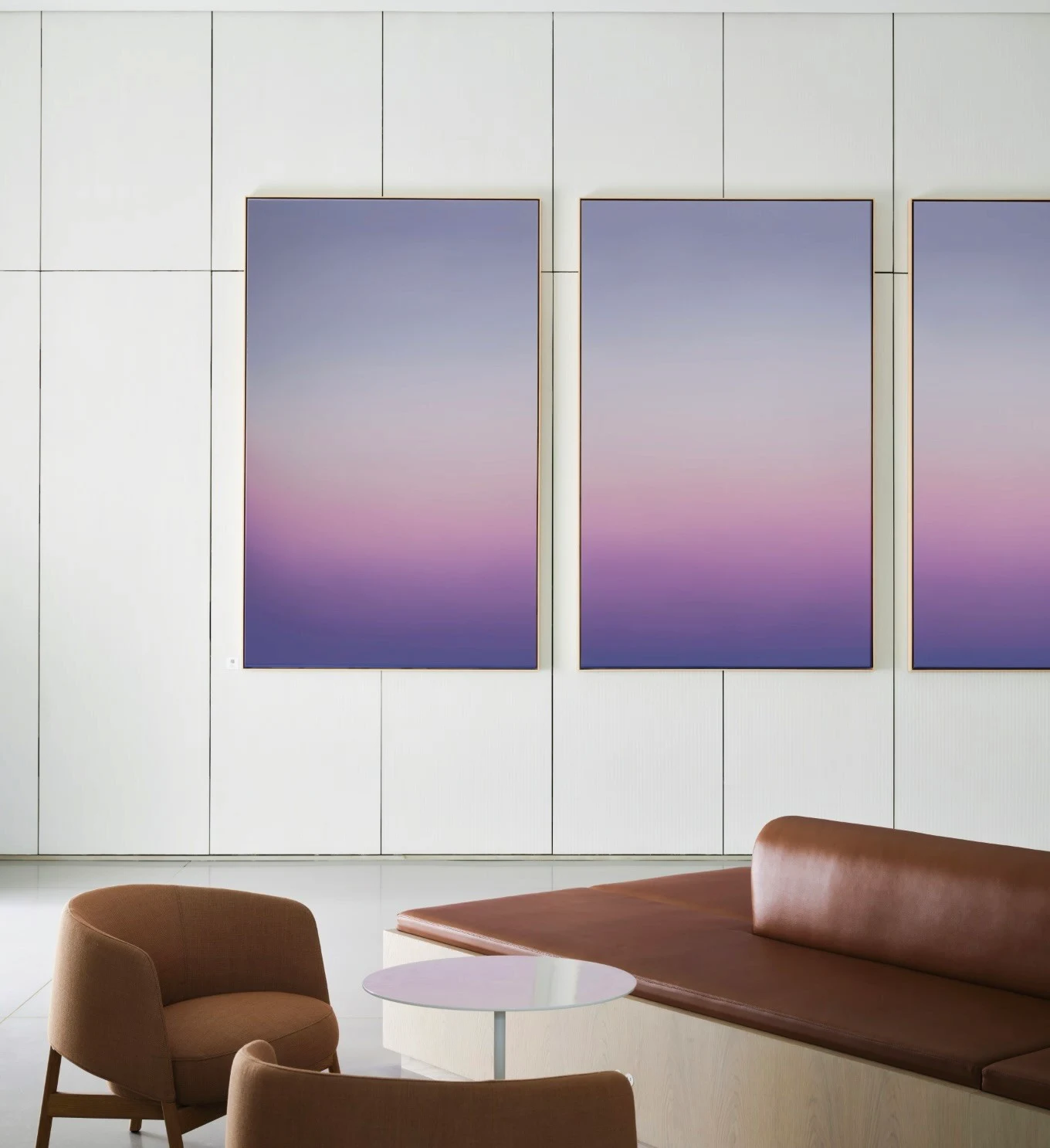 A row of tall panels mounted on a white wall, each holding the same lavender-to-pink gradient, above a leather banquette and low table.