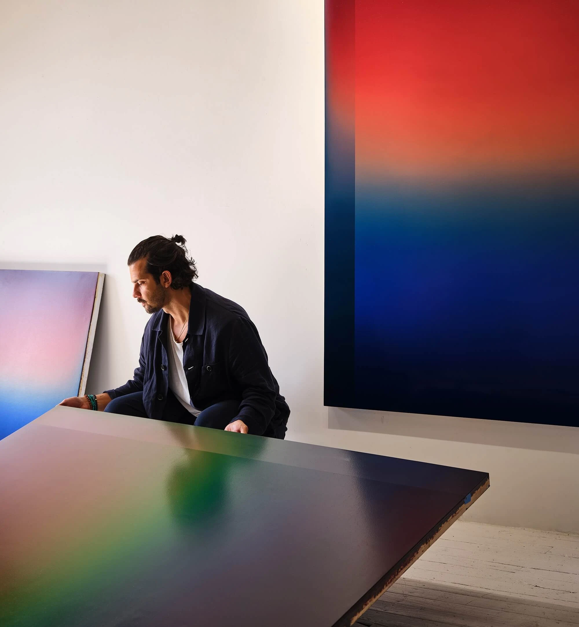 Theo Pinto leaning over a large panel laid flat on a table, a tall canvas of red above deep blue behind him.