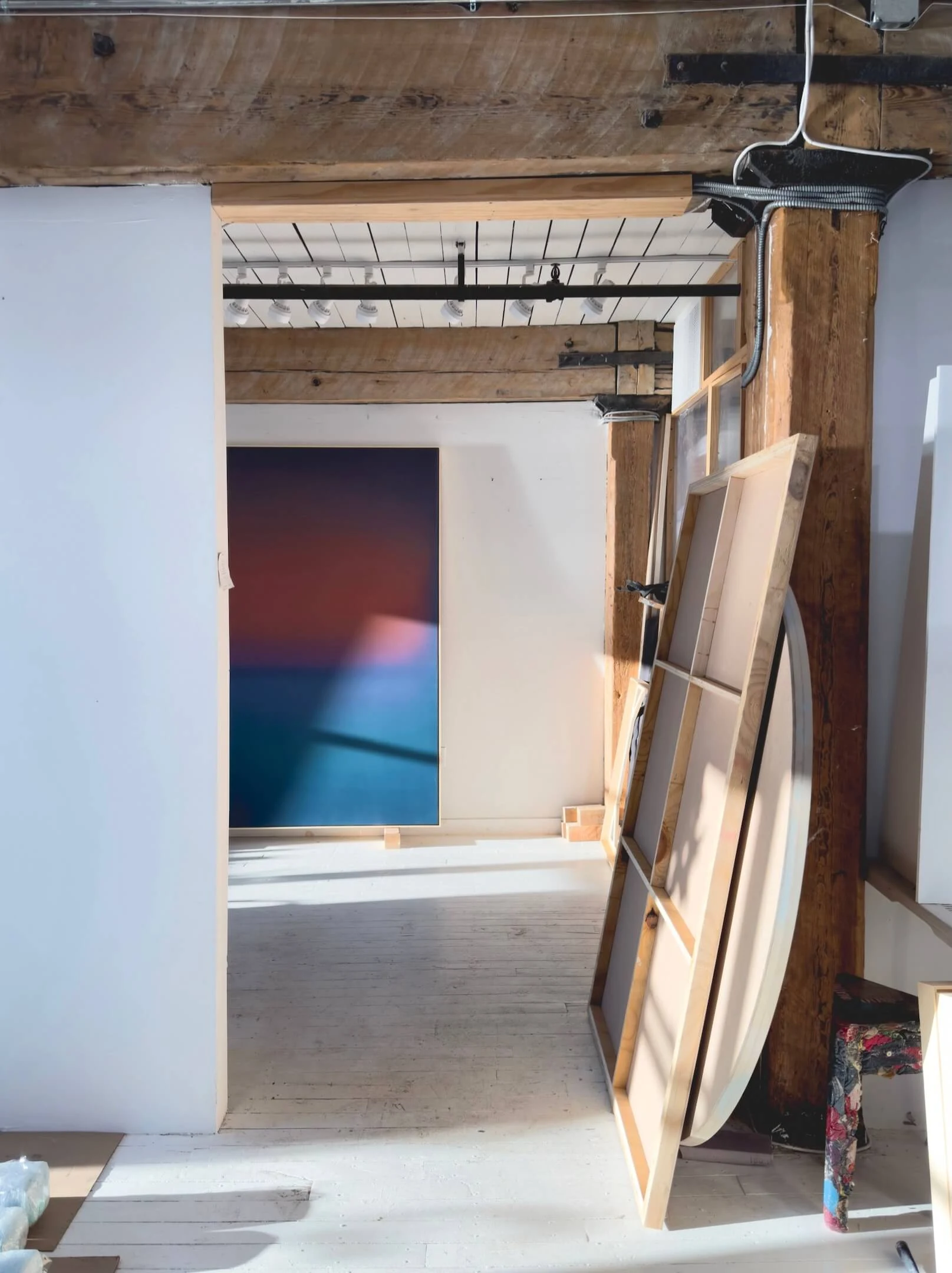 A studio under exposed beams, a painting lit on the far wall and finished panels stacked against the near one.
